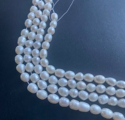 Delicate strands of 6mm freshwater pearl beads elegantly displayed on a smooth black surface.