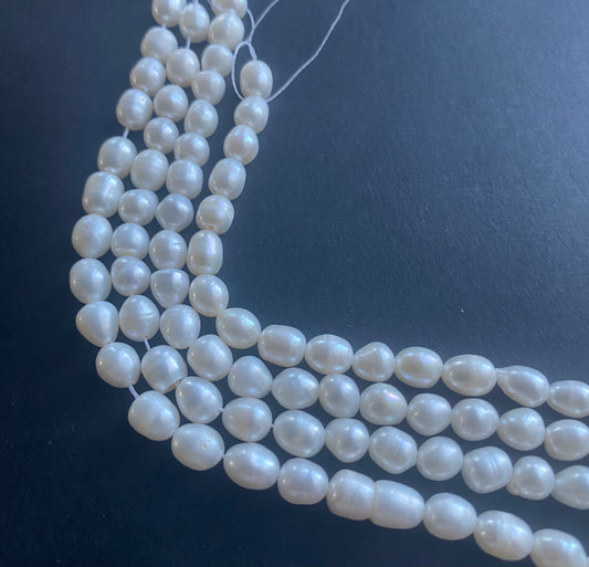 Delicate strands of 6mm freshwater pearl beads elegantly displayed on a smooth black surface.