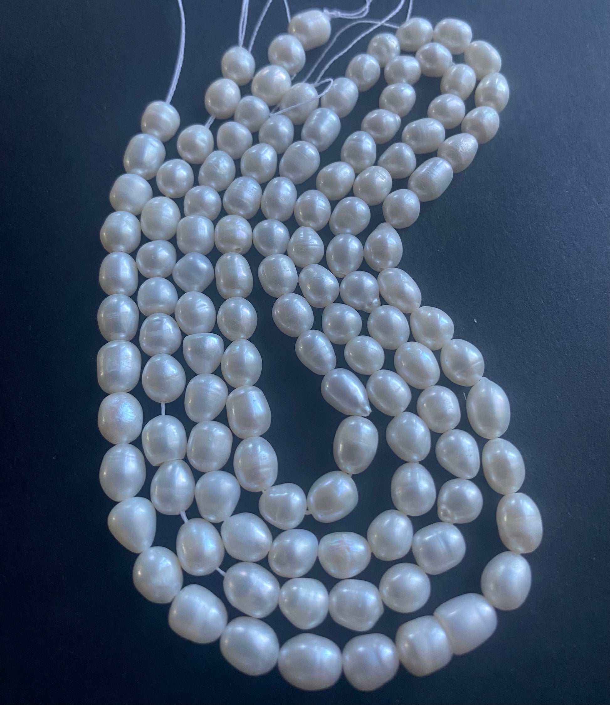 A strand of lustrous 6mm freshwater pearl beads laid out on a dark black surface, highlighting their elegance.