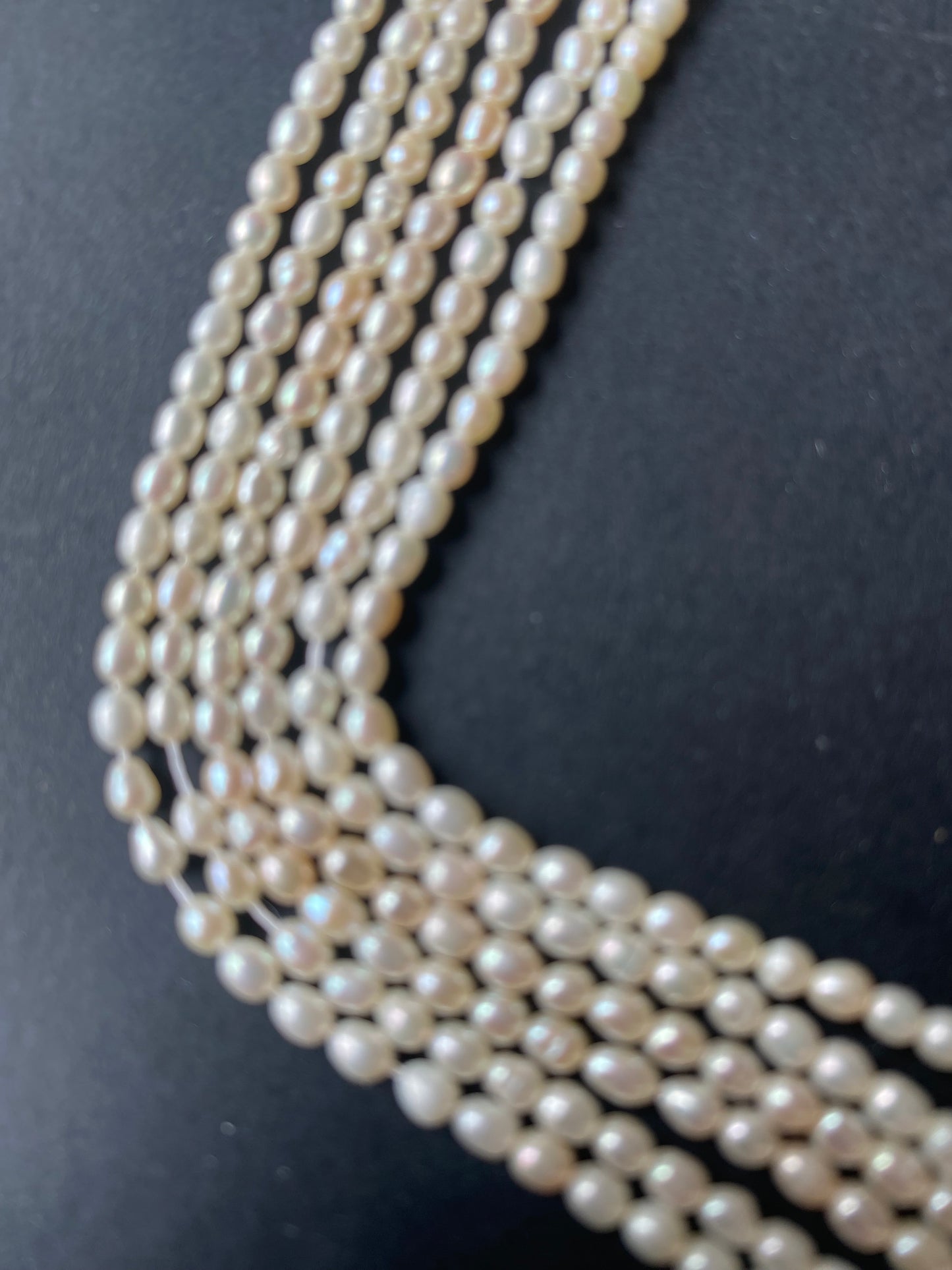 A beautiful strand of 2.7mm freshwater rice pearls resting on a sleek black background, showcasing their lustre