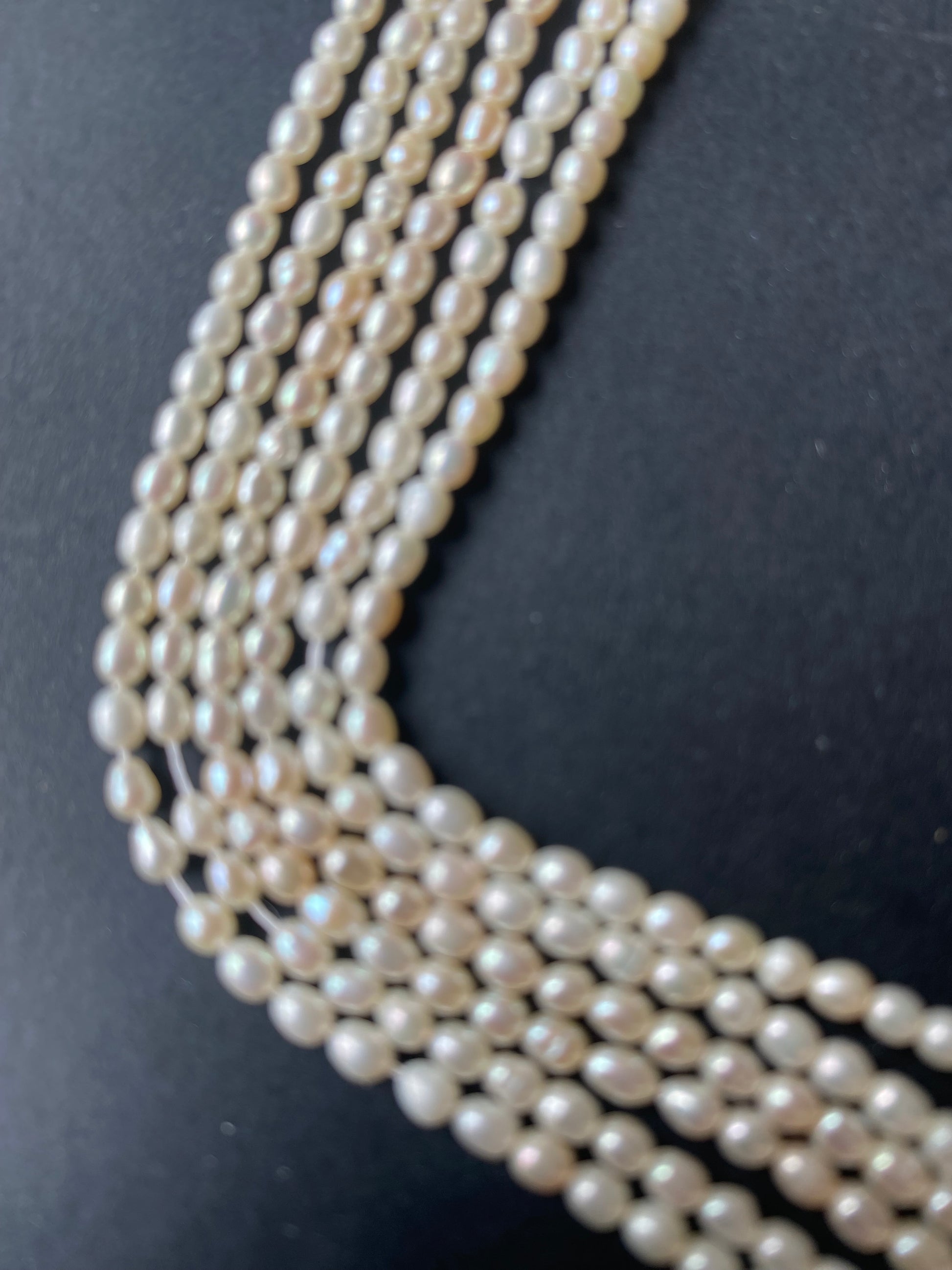 A beautiful strand of 2.7mm freshwater rice pearls resting on a sleek black background, showcasing their lustre