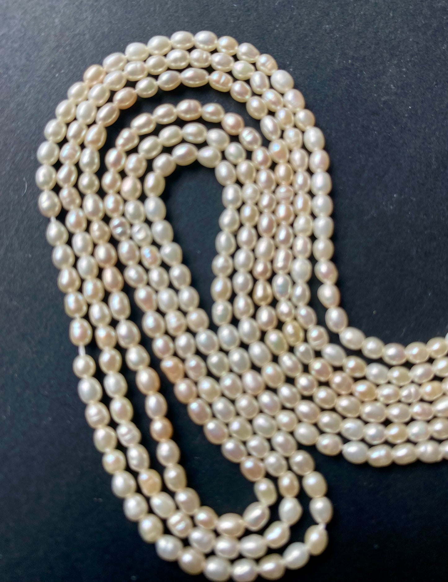 A strand of lustrous 2.7mm freshwater rice pearls laid out on a dark black surface, highlighting their elegance.