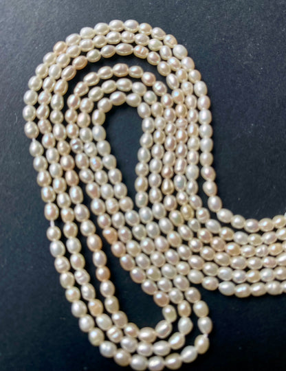 A strand of lustrous 2.7mm freshwater rice pearls laid out on a dark black surface, highlighting their elegance.