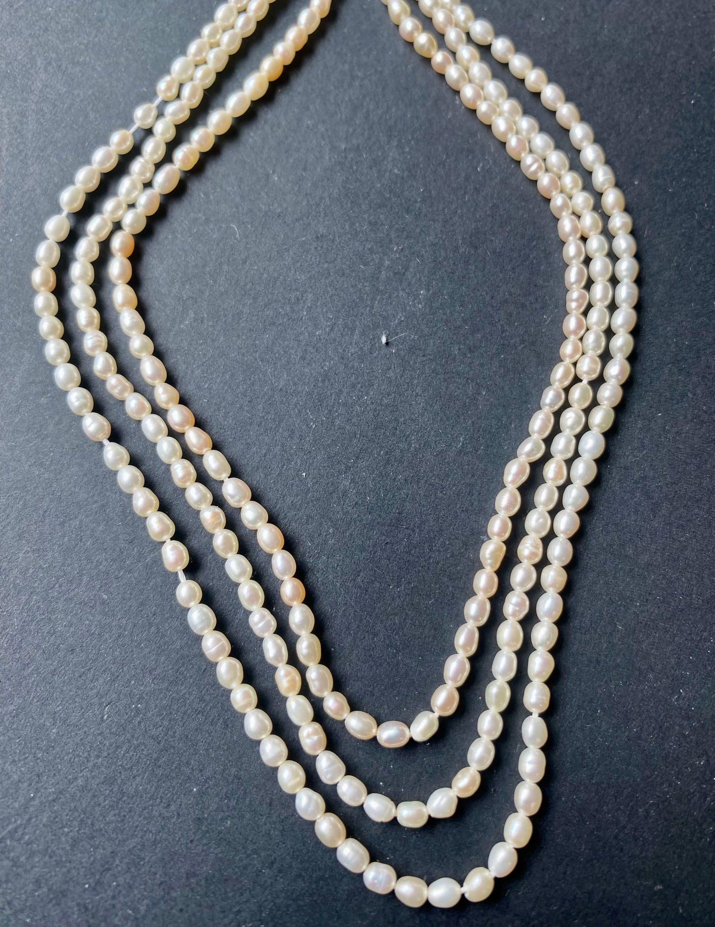 Delicate strands of 2.7mm freshwater rice pearls elegantly displayed on a smooth black surface.