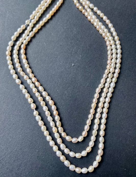 Delicate strands of 2.7mm freshwater rice pearls elegantly displayed on a smooth black surface.