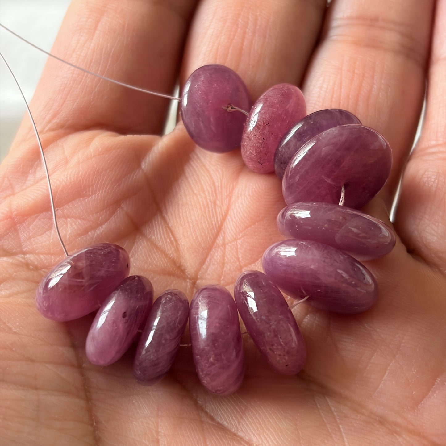A person holds delicate strands of ruby beads, showcasing their smooth design.