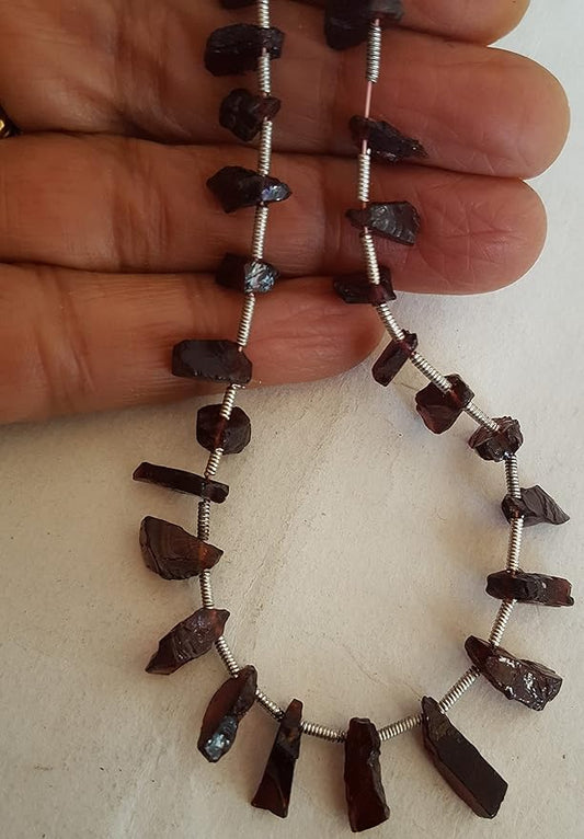 A hand holding a cluster of garnet gemstone beads, showcasing their rough texture and vibrant colour.