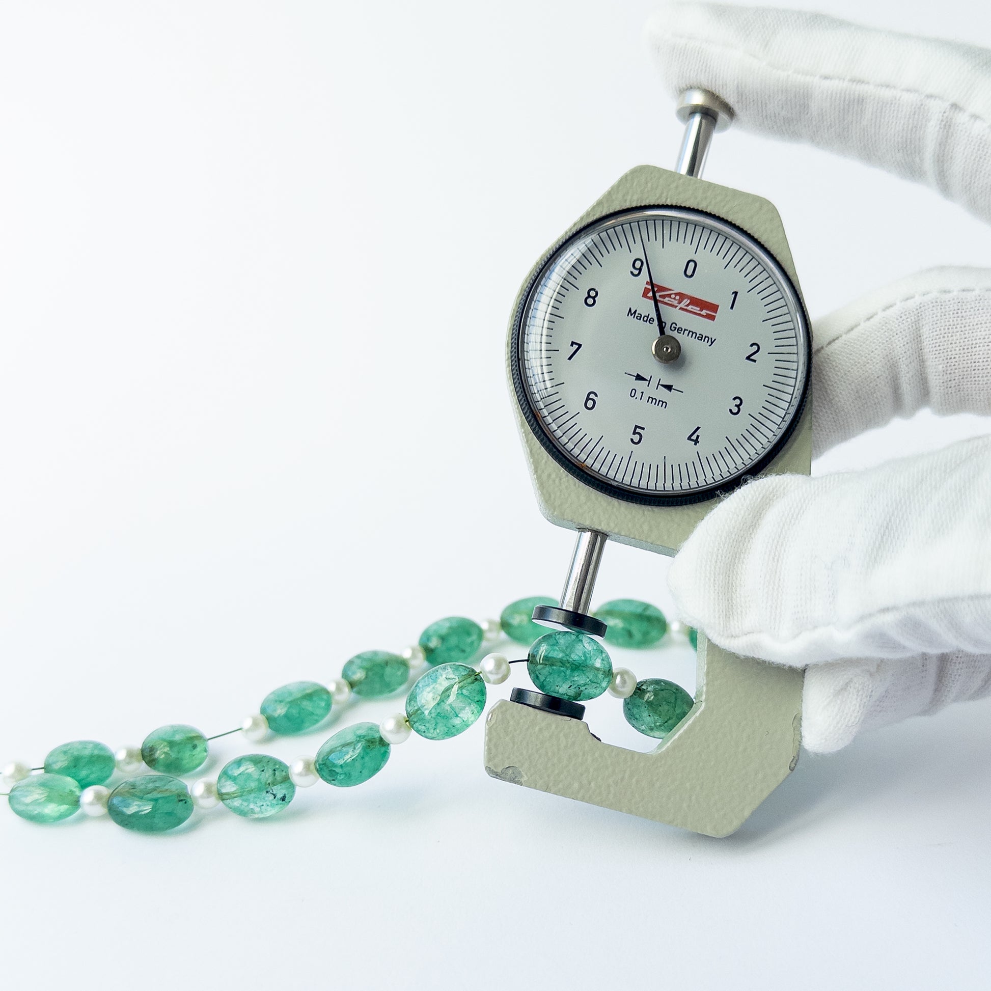 A dial gauge measures the Green Beryl and Shell Pearl smooth oval 9.5–12mm gemstone.