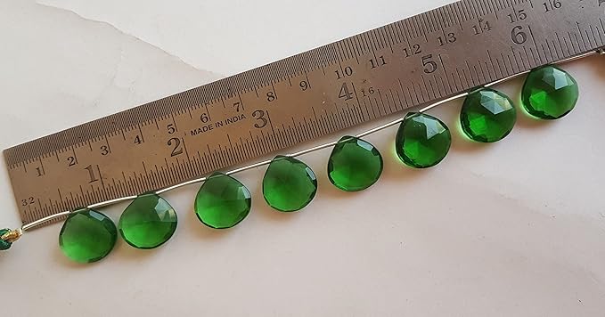 A ruler alongside a strand adorned with faceted heart shaped green hydro beads, showcasing their delicate design.
