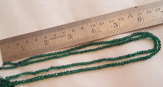 A ruler beside a cluster of green onyx gemstone beads, measuring their size.