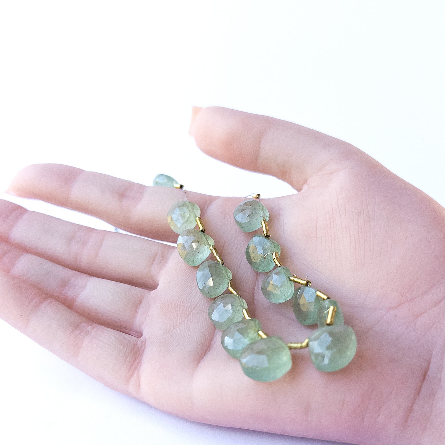 A person holds delicate pieces of Green Strawberry Quartz beads, showcasing their faceted briolette design.