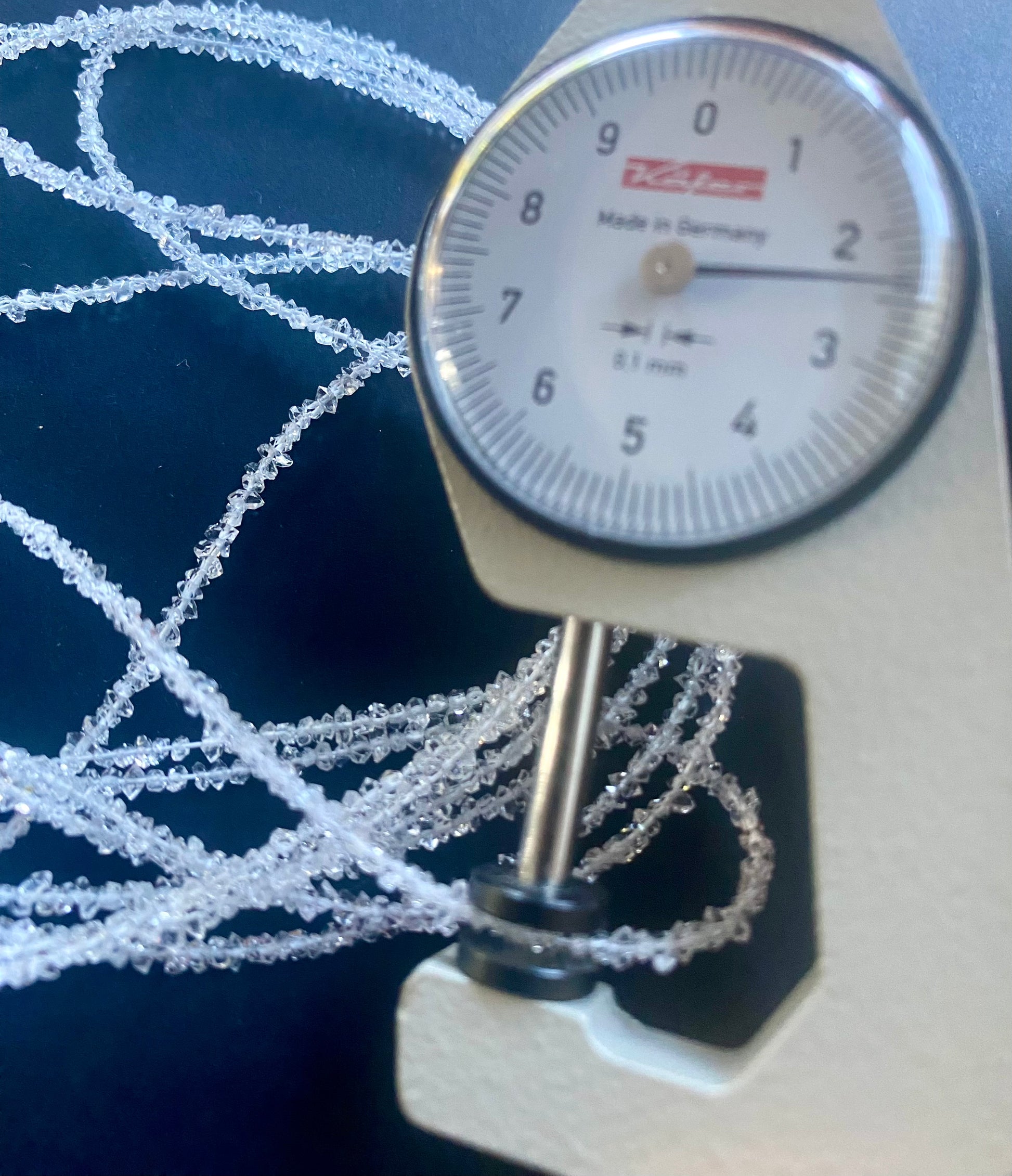 A dial gauge  next to natural Herkimer Diamond nugget  gemstone beads, measuring 2mm to 2.5mm  in diameter.
