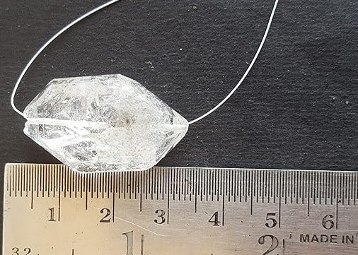 A Herkimer Diamond with a rough centre drilled bead rests on a ruler, showcasing its clarity and unique shape.