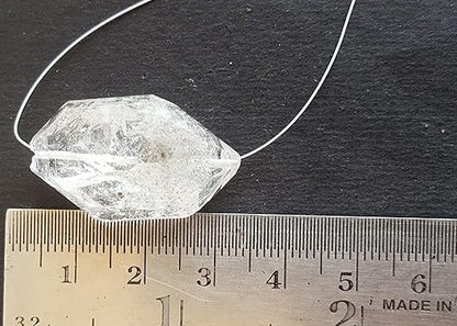 A Herkimer Diamond with a rough centre drilled bead rests on a ruler, showcasing its clarity and unique shape.