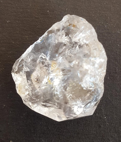  A Herkimer diamond stone bead on a table, featuring its unpolished surface and striking clarity, capturing light beautifully.