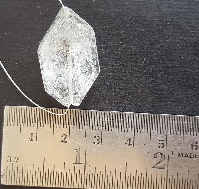  A clear Herkimer Diamond with a rough centre drilled bead is placed on a ruler, highlighting its sparkling clarity.
