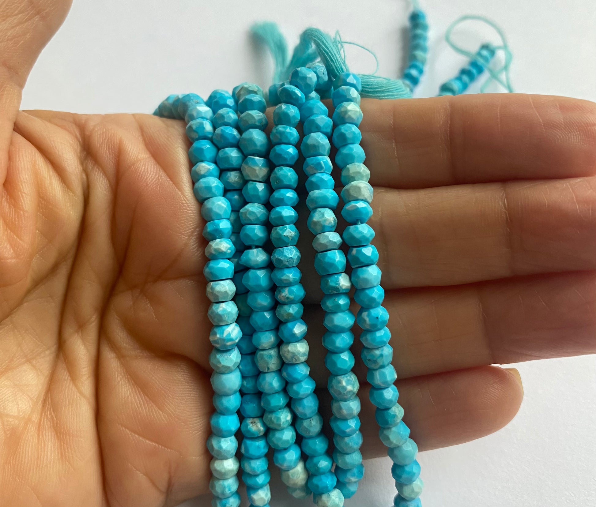 A hand holds a stunning blue strand made of faceted Howlite Turquoise rondelle gemstones.