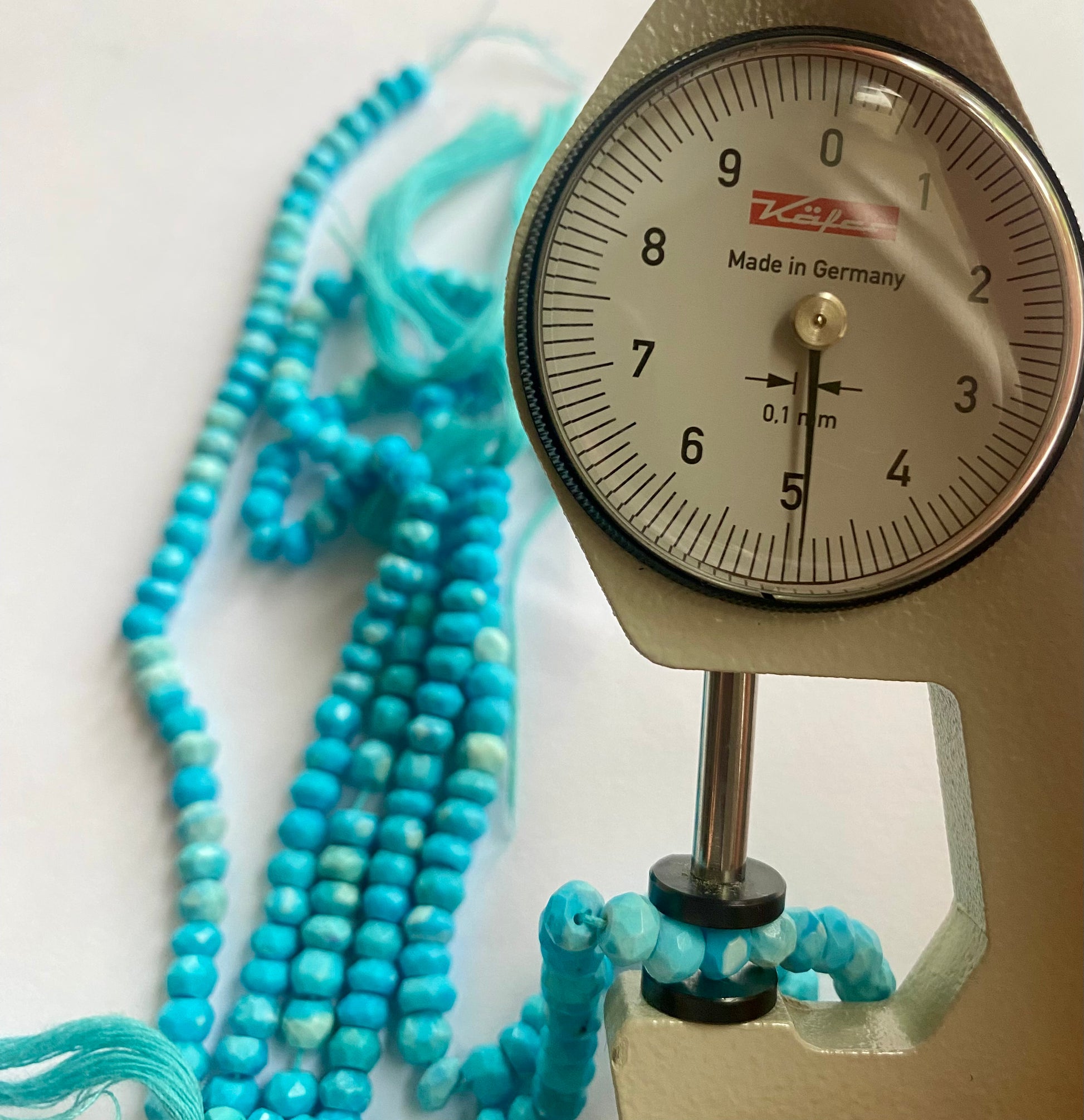 A dial gauge measures the howlite turquoise faceted rondelle gemstone.