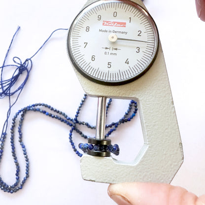 A dial gauge measures the Lapis Lazuli faceted rondelle 2.5mm gemstone for quality assurance.