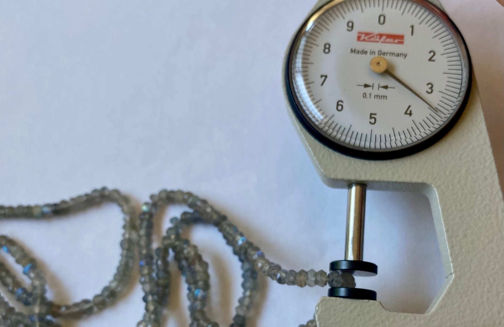 A dial gauge displaying a metallic hues beside the gemstone strand made of faceted rondelle Labradorite beads, 3.5mm in size.