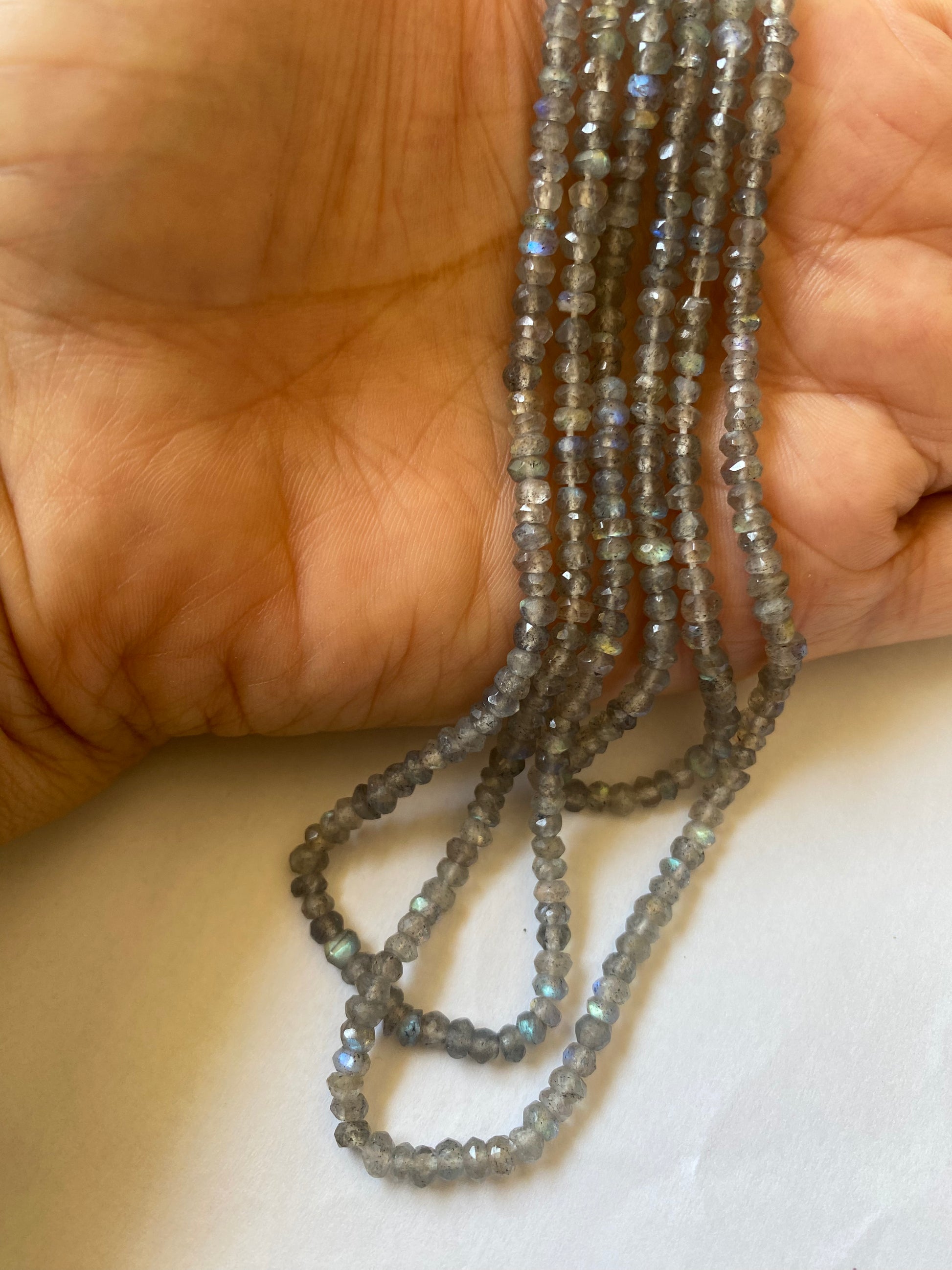 A person holding a strand of Labradorite faceted rondelle beads, measuring 3.5mm in size.