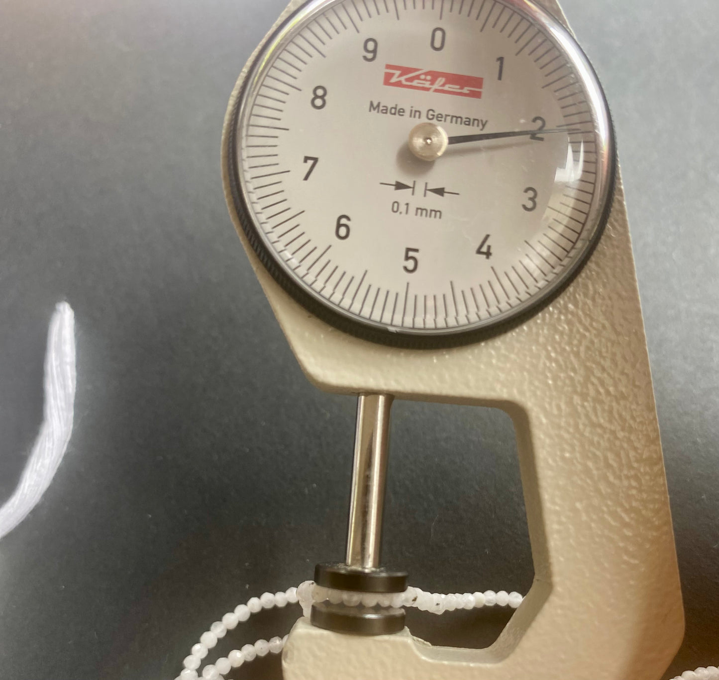 A dial gauge measures the Moonstone Faceted Rondelle 2.1mm gemstone.