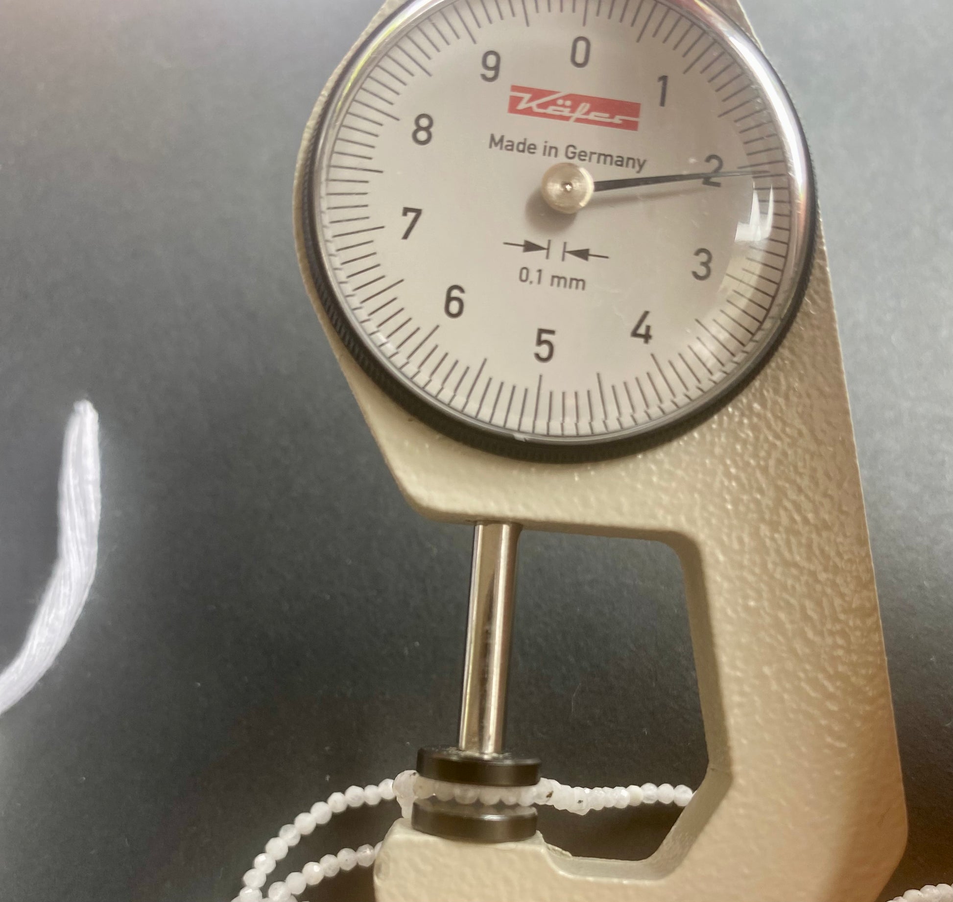 A dial gauge measures the Moonstone Faceted Rondelle 2.1mm gemstone.