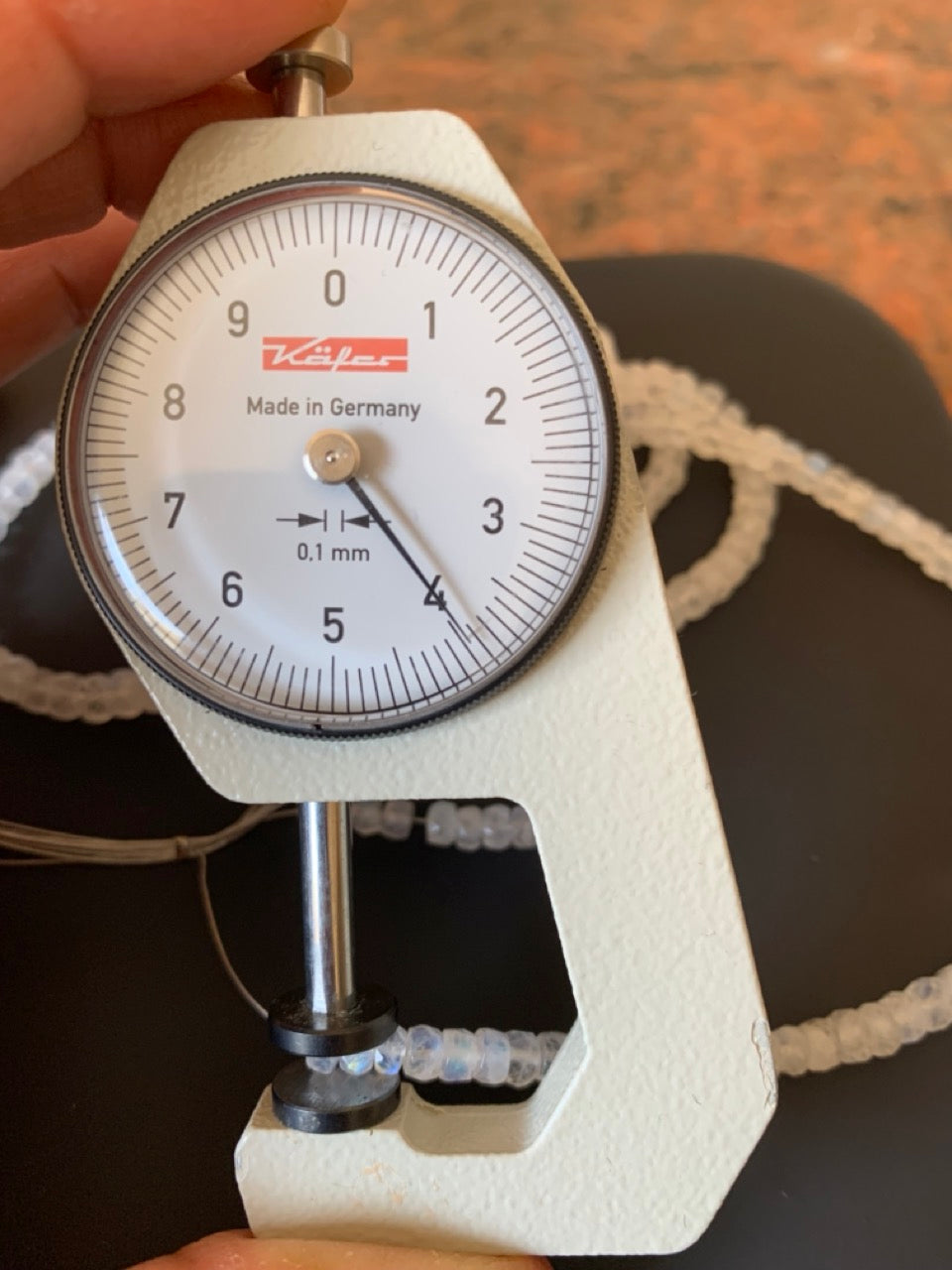 A dial gauge next to an array of colourful moonstone beads, showcasing their size and measurement.