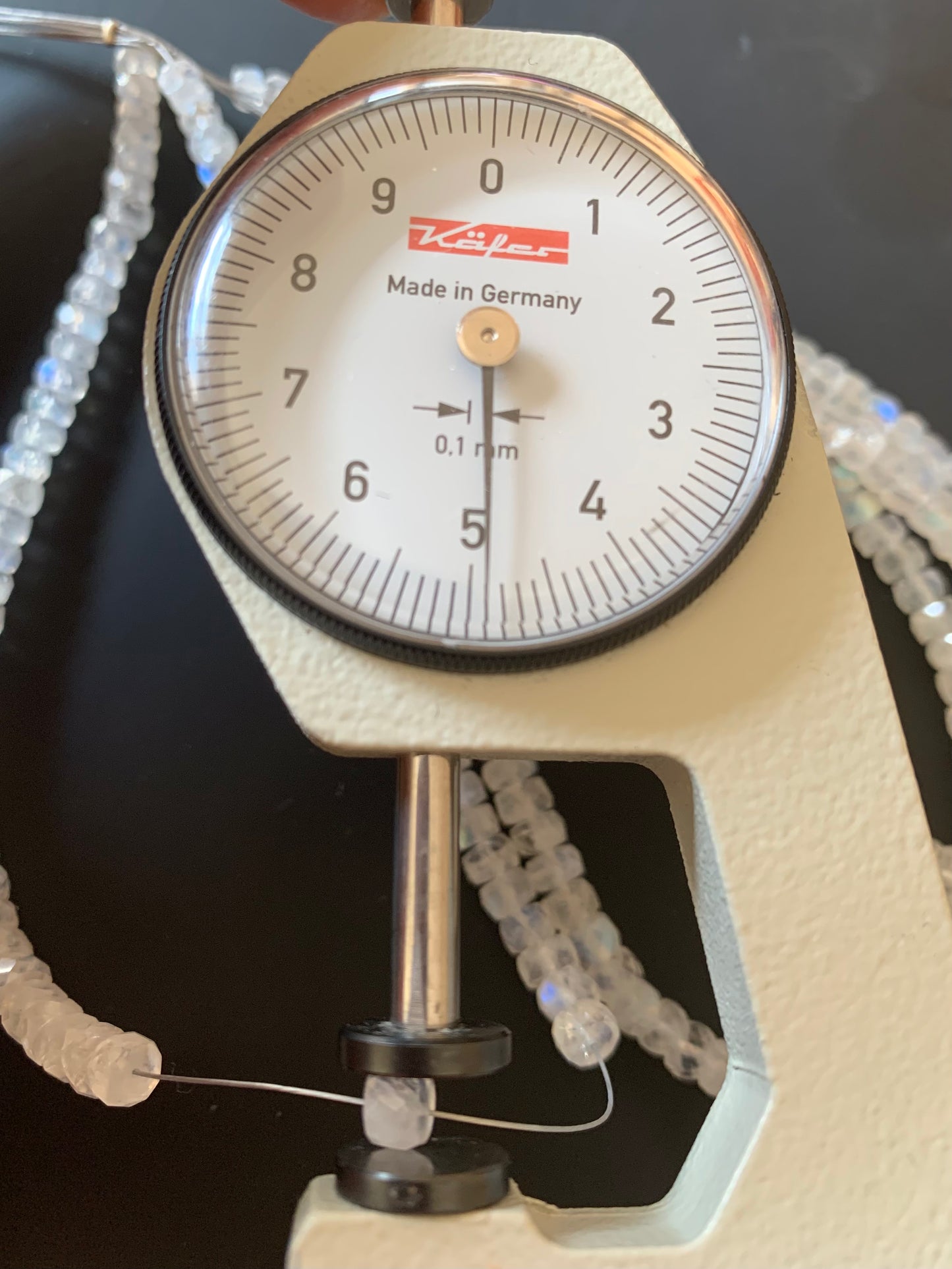 Close-up of a measuring dial gauge alongside a vibrant collection of 4mm to 5mm moonstone gemstone beads.