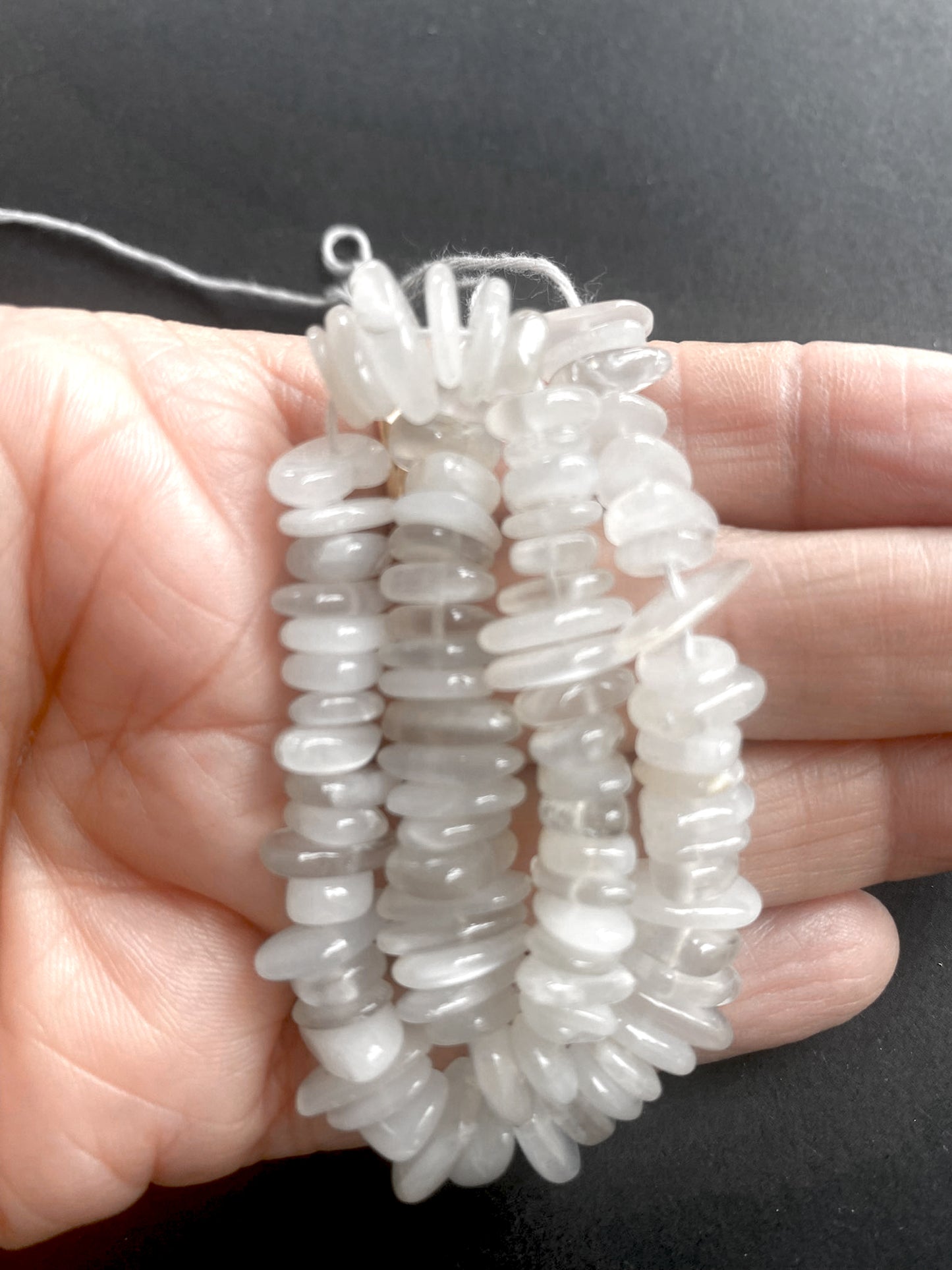 A person gently holds strands of Moonstone beads, showcasing their smooth, radiant finish and delicate beauty