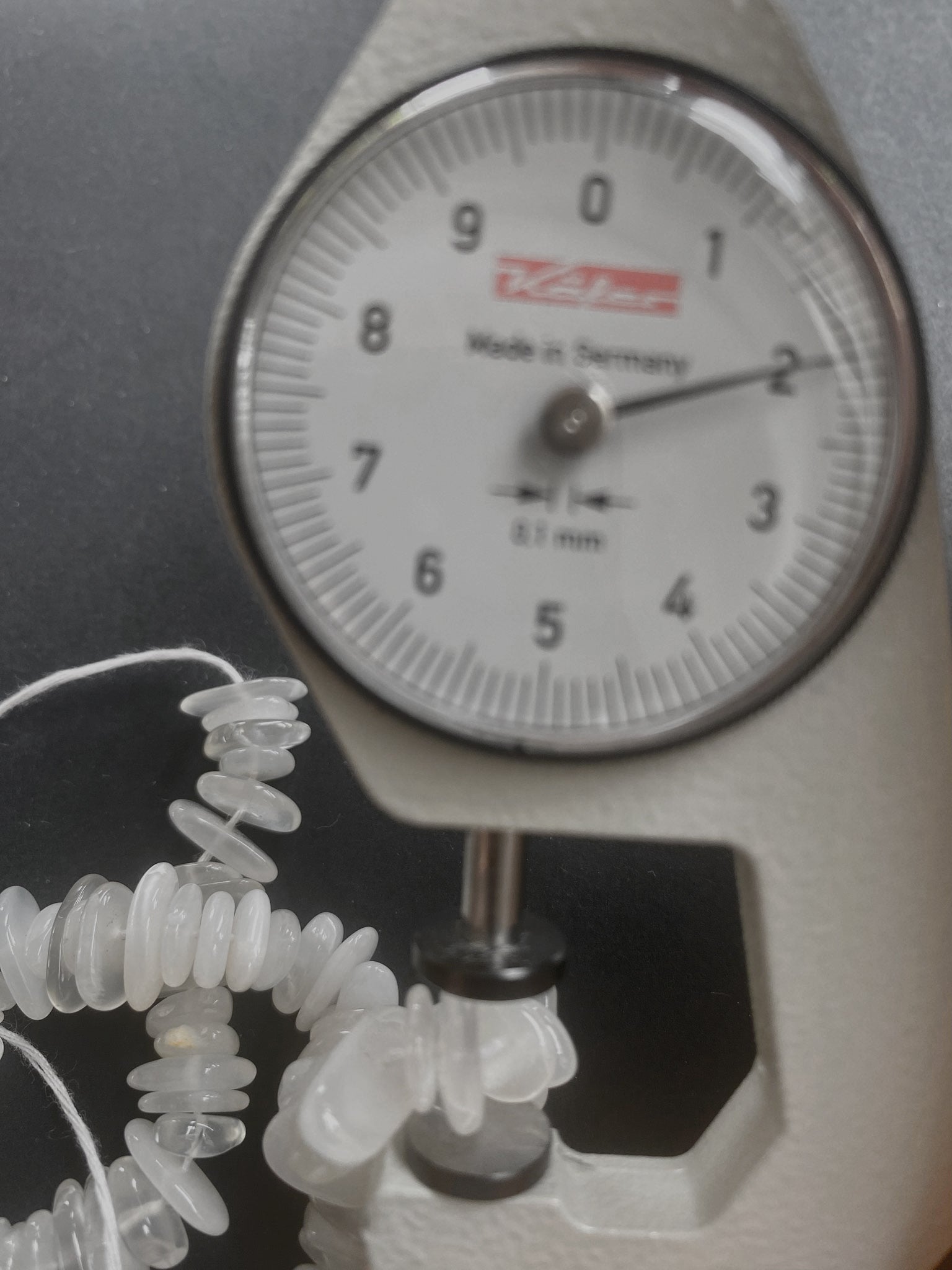 A dial gauge measures the Moonstone smooth chip 8-12mm gemstone, ensuring precise sizing.