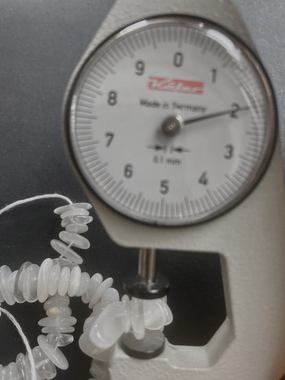A dial gauge measures the Moonstone smooth chip 8-12mm gemstone, ensuring precise sizing.