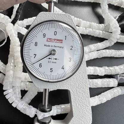 A dial gauge measures the Moonstone smooth wheel gemstone beads, ensuring precise 7.0-7.1mm sizing.