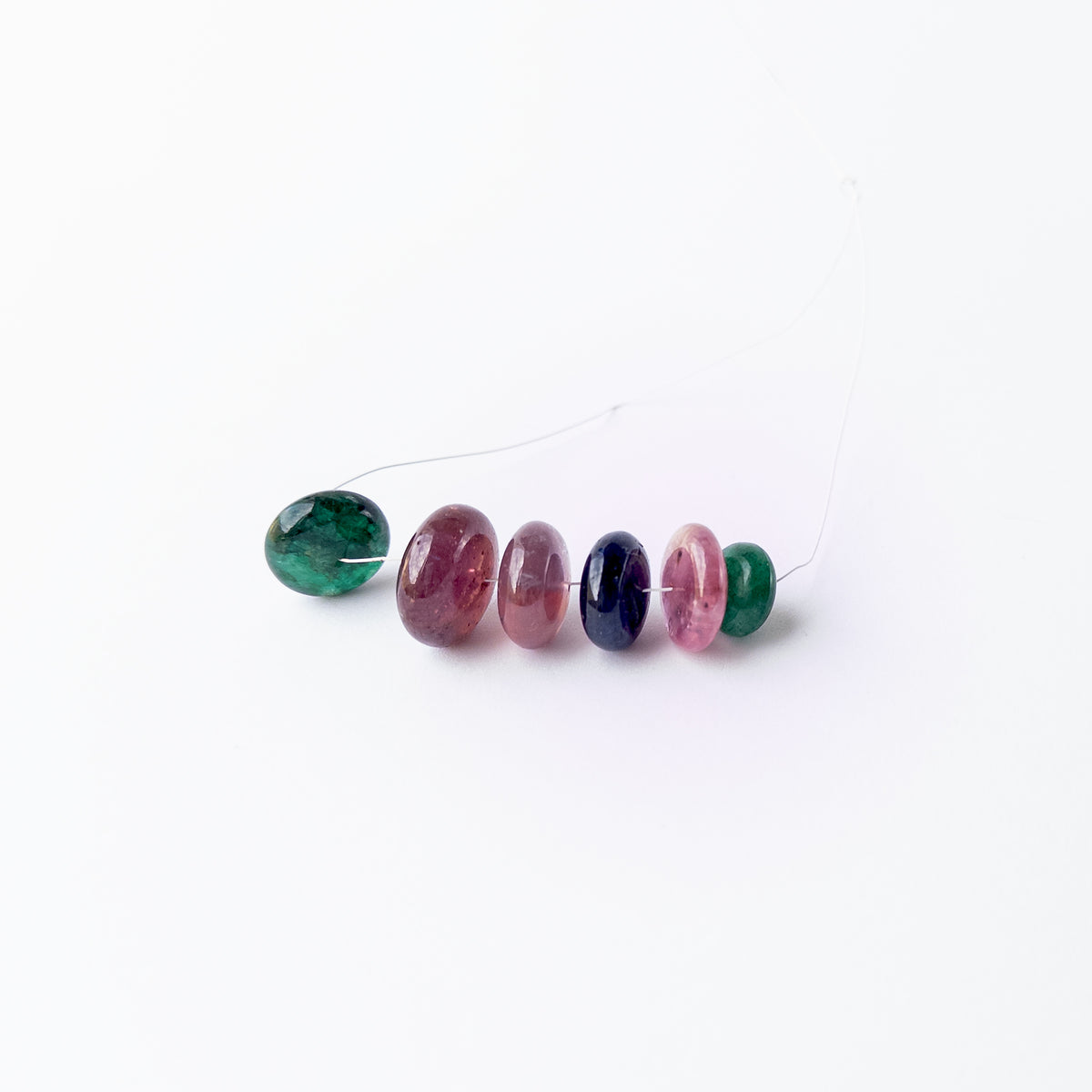 Multi‑precious Emerald, Ruby and Blue Sapphire smooth rondelle beads arranged together, showcasing rich colour and polished shine.