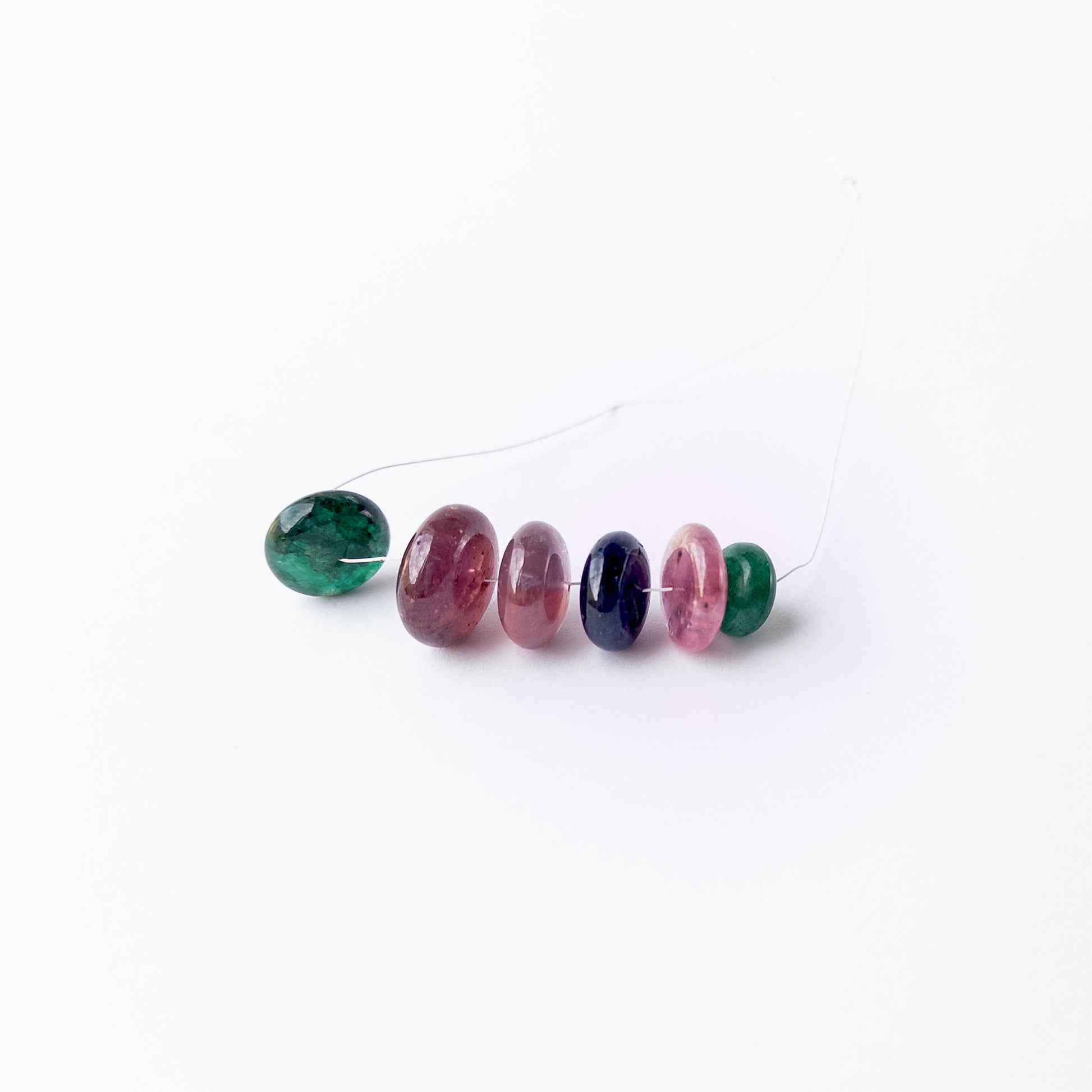 Multi‑precious Emerald, Ruby and Blue Sapphire smooth rondelle beads arranged together, showcasing rich colour and polished shine.