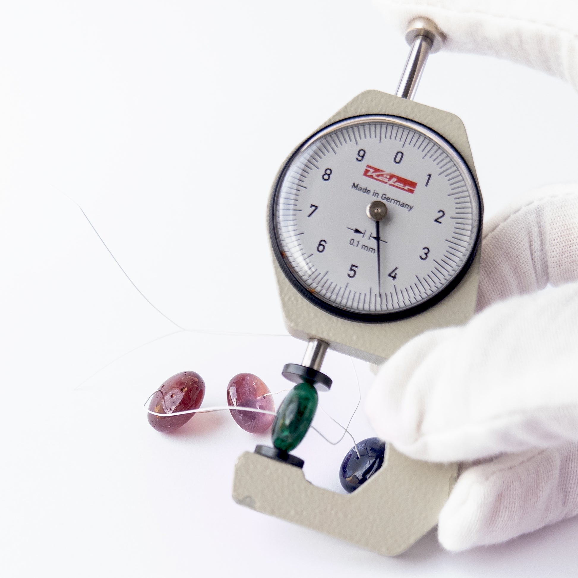 A dial gauge measures the Emerald, Ruby and Blue Sapphire smooth rondelle 10.7–16.3mm gemstone.