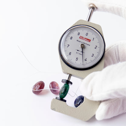 A dial gauge measures the Emerald, Ruby and Blue Sapphire smooth rondelle 10.7–16.3mm gemstone.