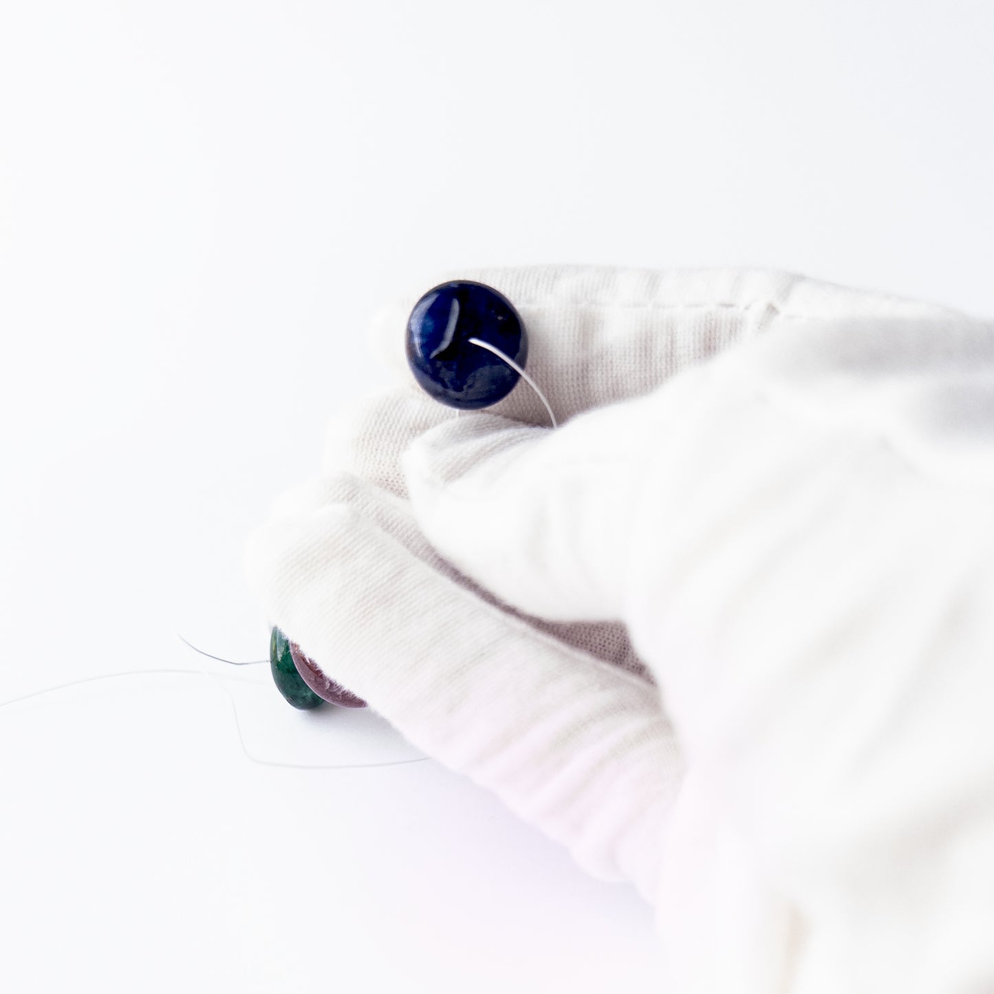 A person holds delicate pieces o Blue Sapphire beads, showcasing their smooth rondelle design.