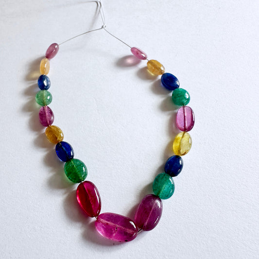 Smooth oval multi precious beads featuring ruby, sapphire, and emerald with vibrant shine and polished finish.