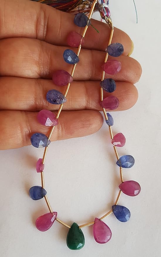A person holds a vibrant bunch of multi-coloured faceted beads, including ruby, blue sapphire, and emerald.