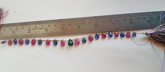 Close-up of a ruler beside colourful multi-precious beads, including ruby, blue sapphire, and emerald.