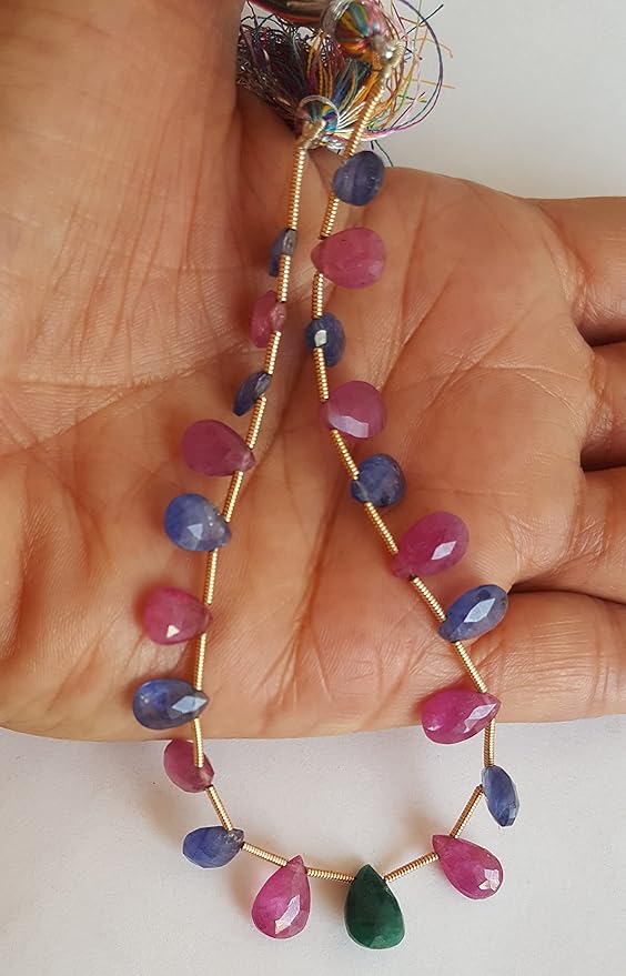A hand displays a colourful assortment of faceted beads, featuring ruby, blue sapphire, and emerald.