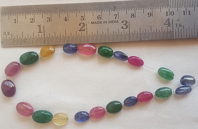 Close-up of a measuring ruler beside colourful multi-precious beads, including ruby, blue sapphire, yellow sapphire, and emerald.