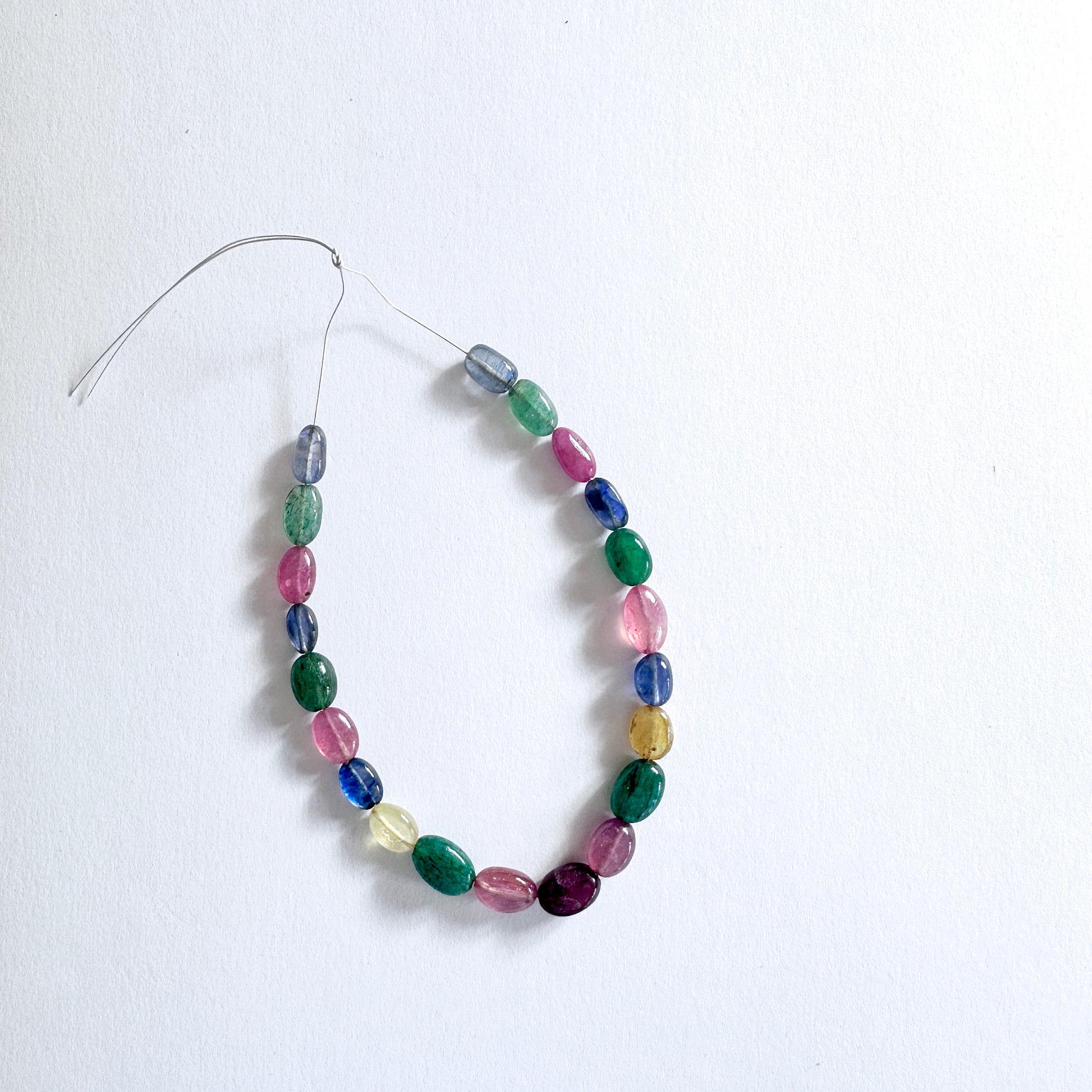 Mixed gemstone beads in oval cut display vivid reds, blues, yellows, and greens with elegant shine.