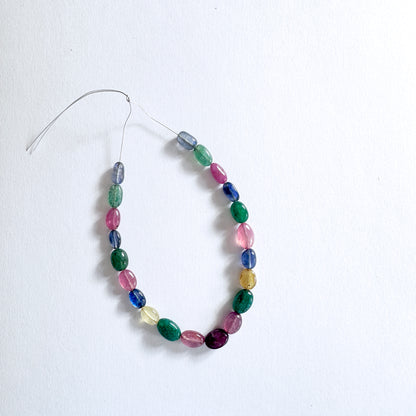 Mixed gemstone beads in oval cut display vivid reds, blues, yellows, and greens with elegant shine.