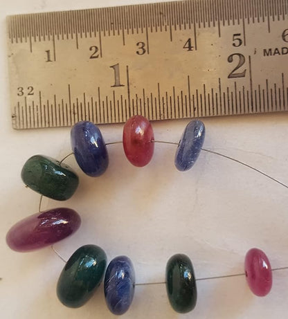 Close-up of a ruler beside colourful multi-precious beads, including ruby, blue sapphire, and emerald.