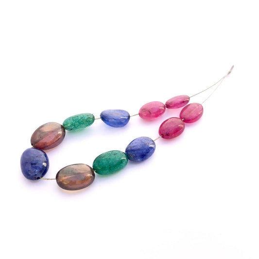 Close‑up of mixed ruby, yellow sapphire, blue sapphire and emerald smooth oval 7–9mm beads showing polished surfaces and vivid colour.
