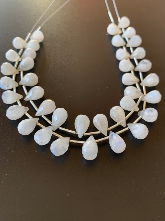Delicate moonstone tear drop faceted beads glimmer on a sleek black background, highlighting their soft, warm hue.