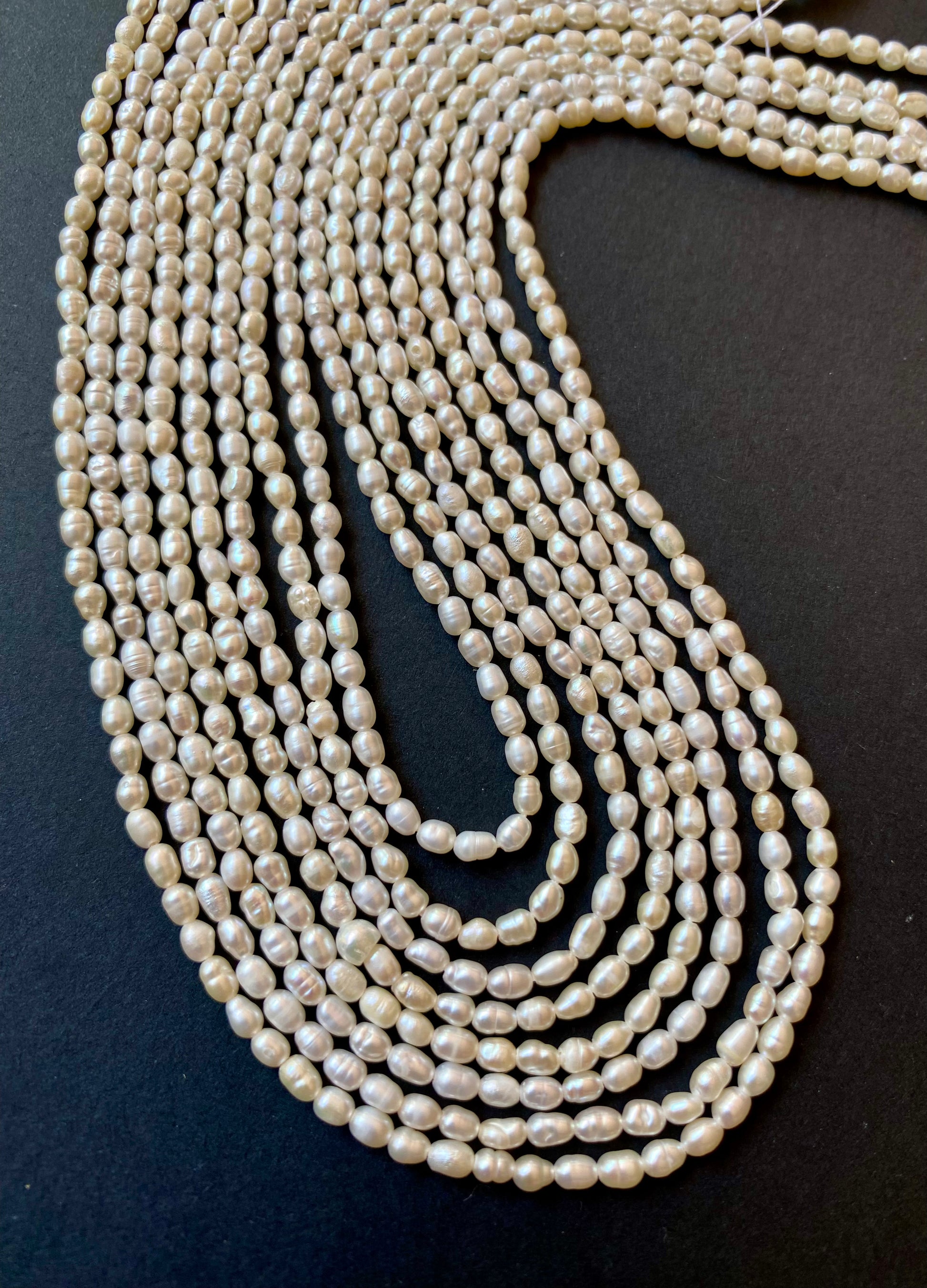 Strands of lustrous  2.5-2.75mm pearl beads laid out on a dark black surface, highlighting their elegance.