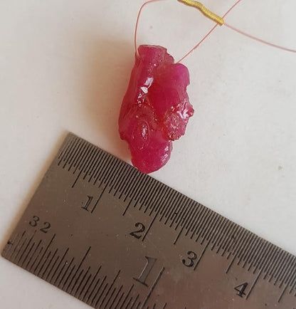 Close-up of a measuring ruler beside colourful precious ruby bead.